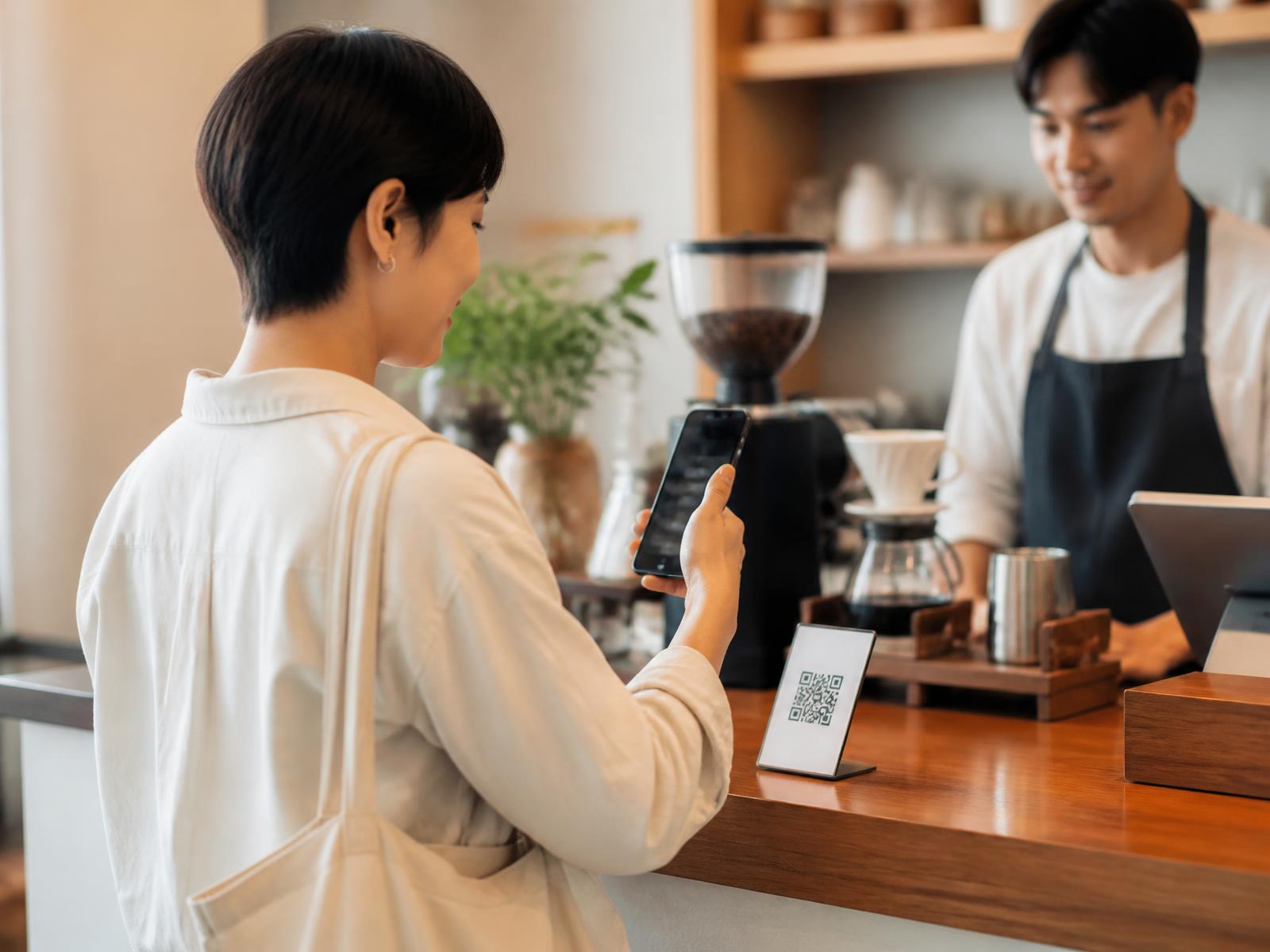 Customer scanning a QR code at a cafe counter with their own phone